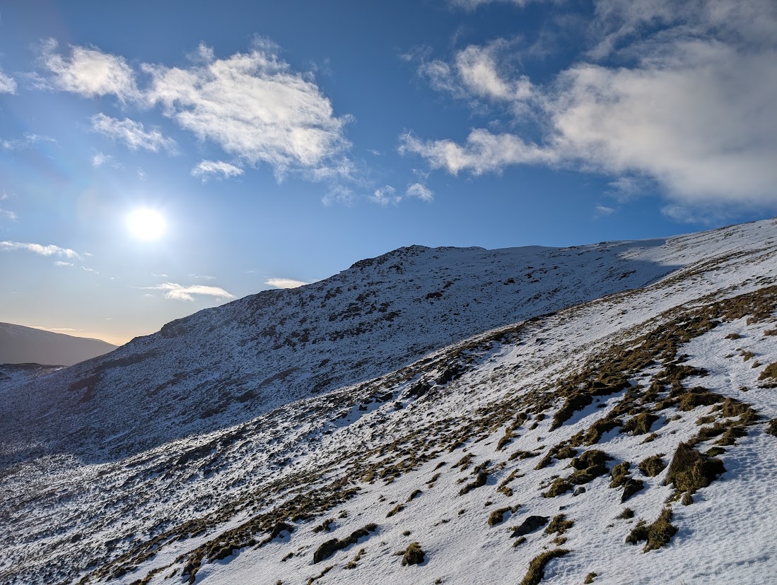 Clough Head under thin, patchy winter snow, with grass and rock showing through, lit by a low winter sun.