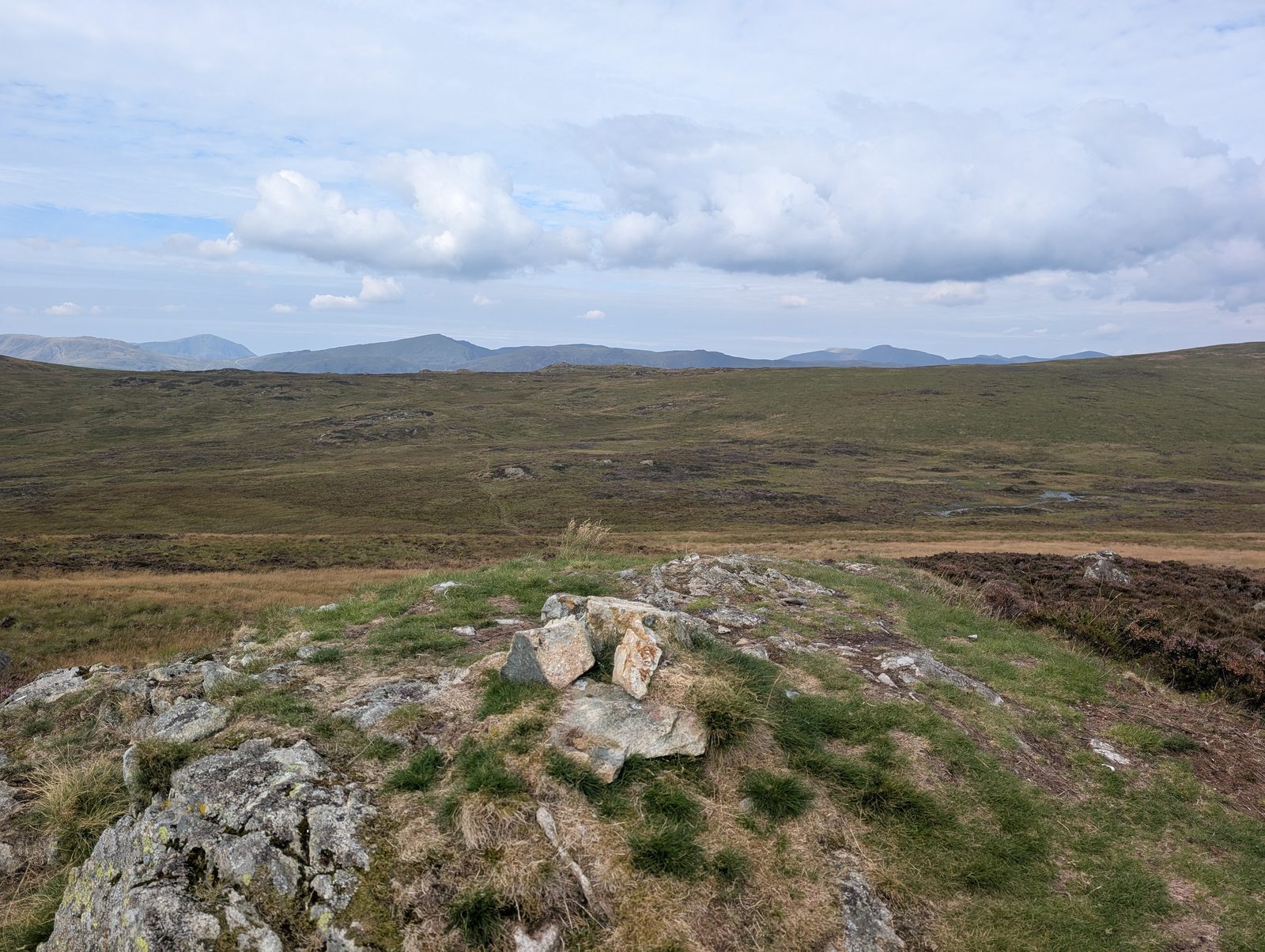 A rocky outcrop with a small cairn on a heathery top, with fells along the distant skyline
