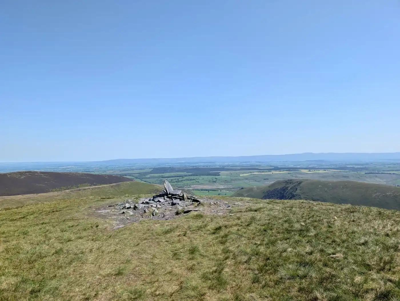 Bannerdale Crags - a low stone cairn on a broad grassy summit, green lowland plains reaching to the far horizon