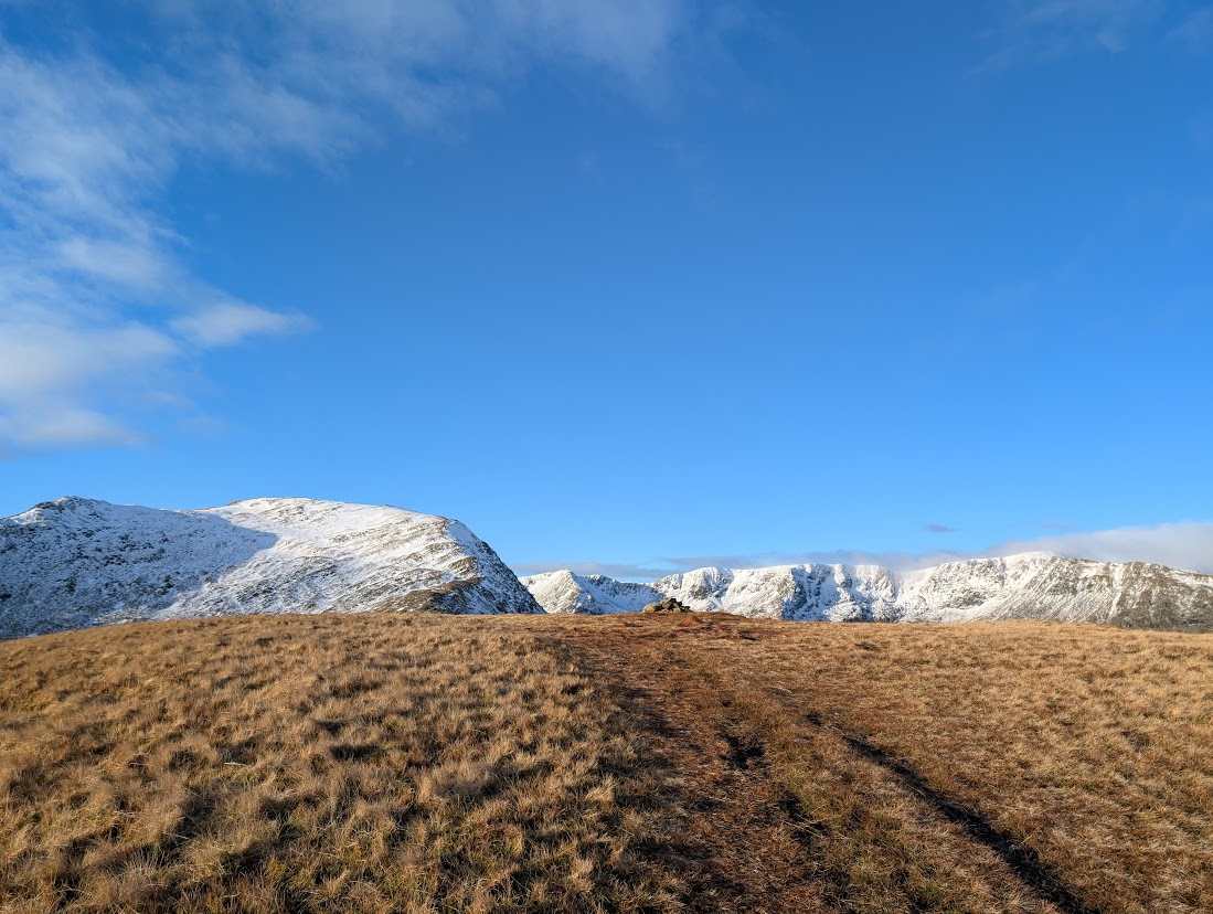 Birks - a faint path over golden grass leading towards snow-covered higher fells under a bright blue sky