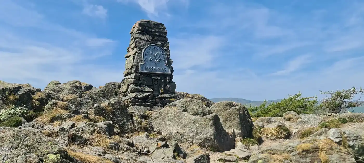 Black Fell - the National Trust stone column on the rocky summit, its 'Black Crag' plaque against a blue sky