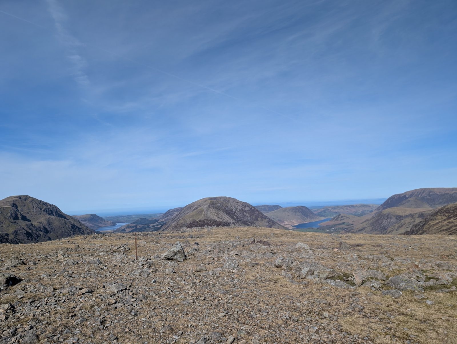 Brandreth - the stony summit plateau with a single fence post, and beyond it a pyramid-shaped fell between two valleys with a lake on either side, under a high blue sky