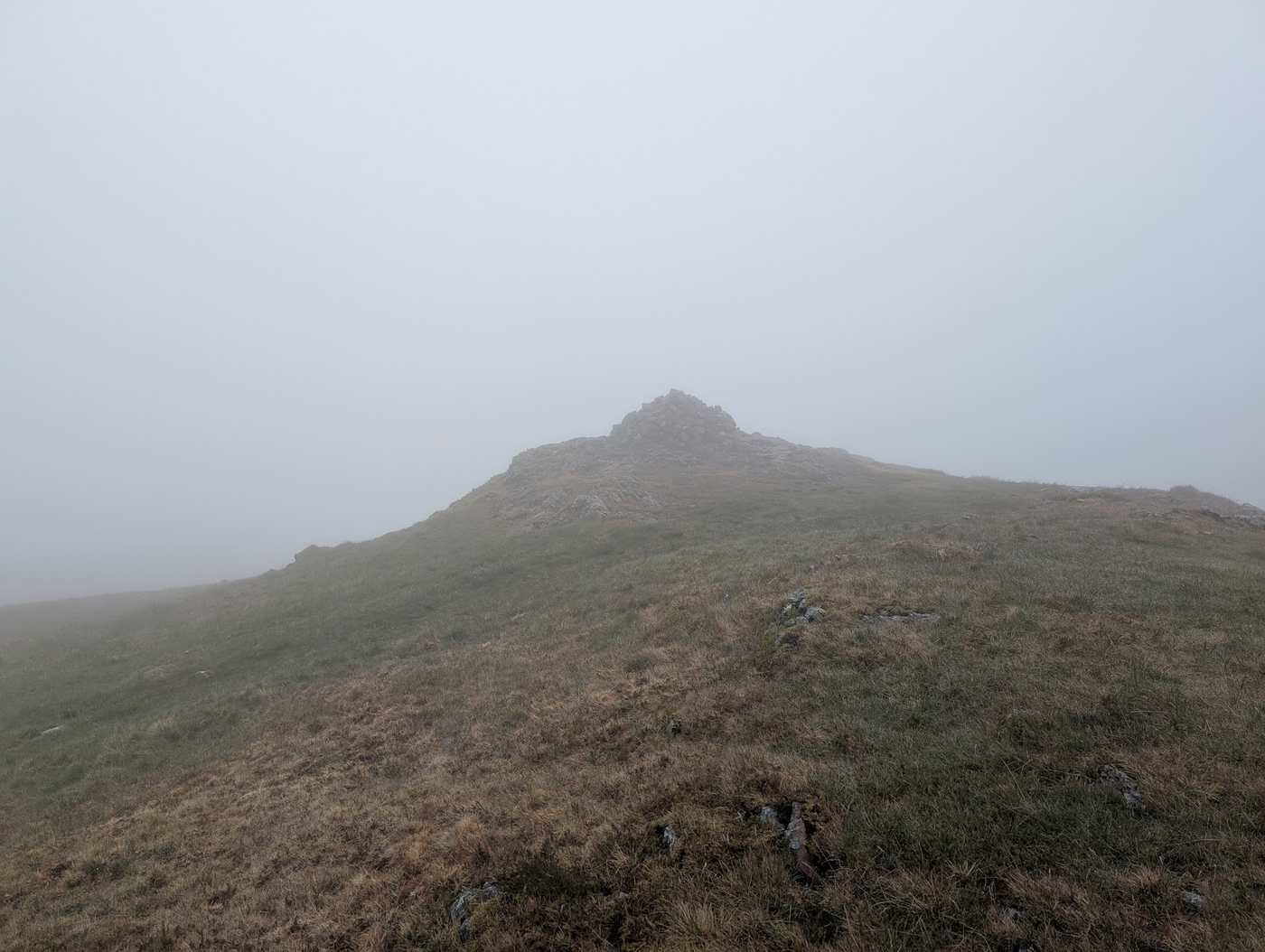 Crag Fell - a rocky summit outcrop emerging from thick mist on a grassy top, visibility low all around