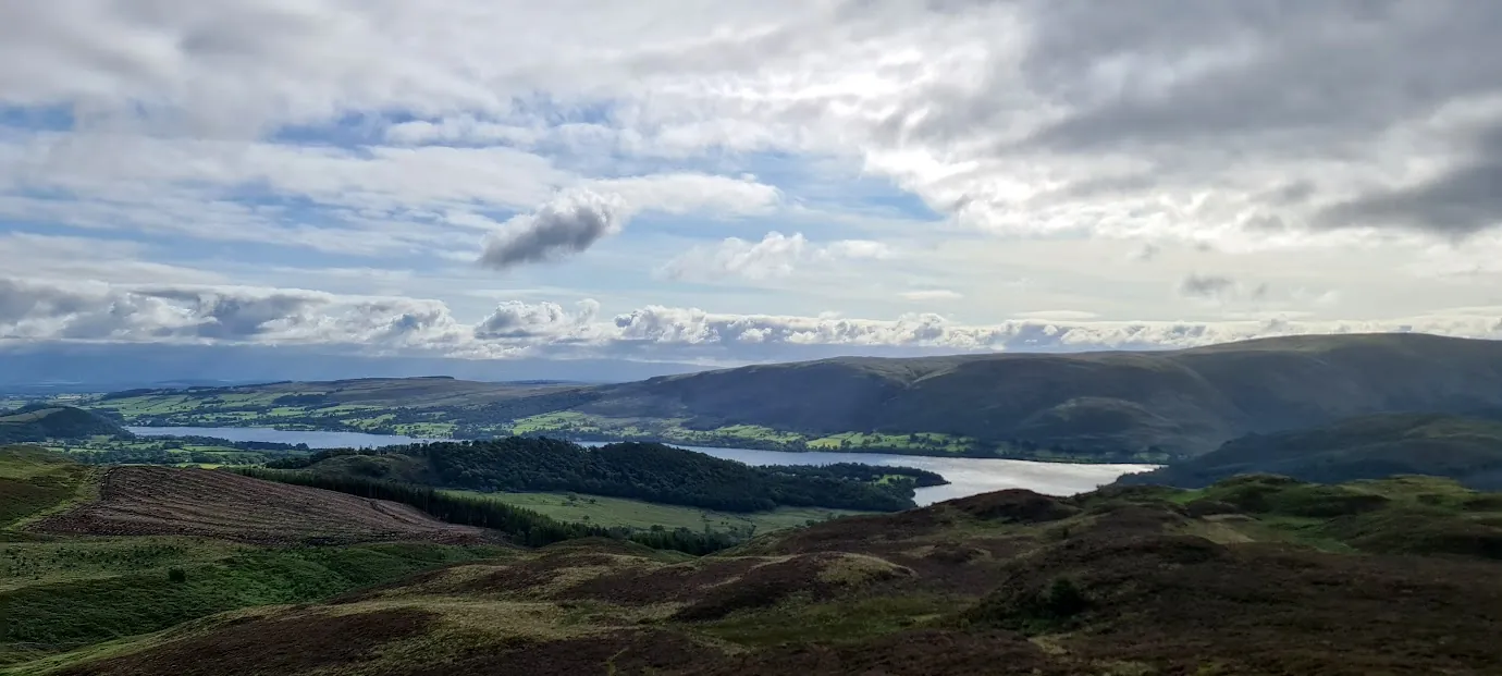Gowbarrow Fell - heathery hummocks falling to Ullswater spread out below, fells and fields under a dramatic cloudy sky