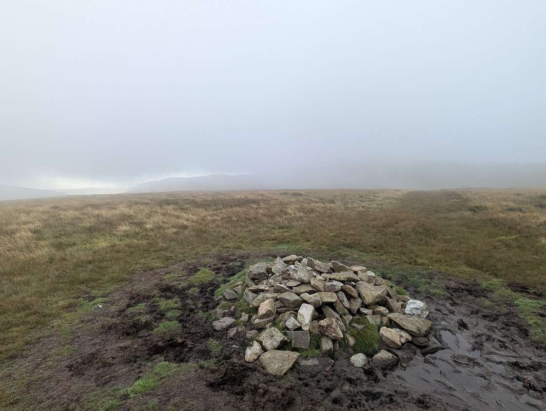Great Sca Fell - a low stone cairn on a boggy moorland top, distant fells dissolving into low cloud