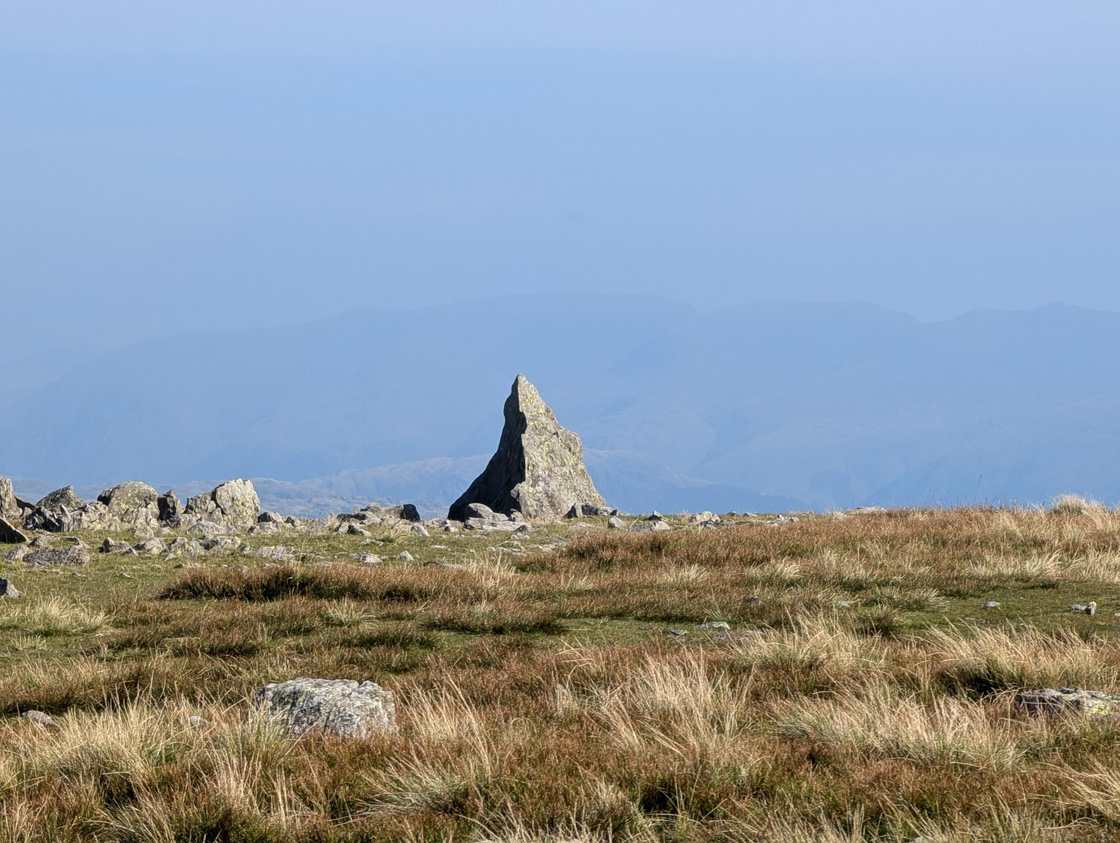 Grey Friar - a distinctive pointed summit rock on grass, with hazy layered fells fading into the distance