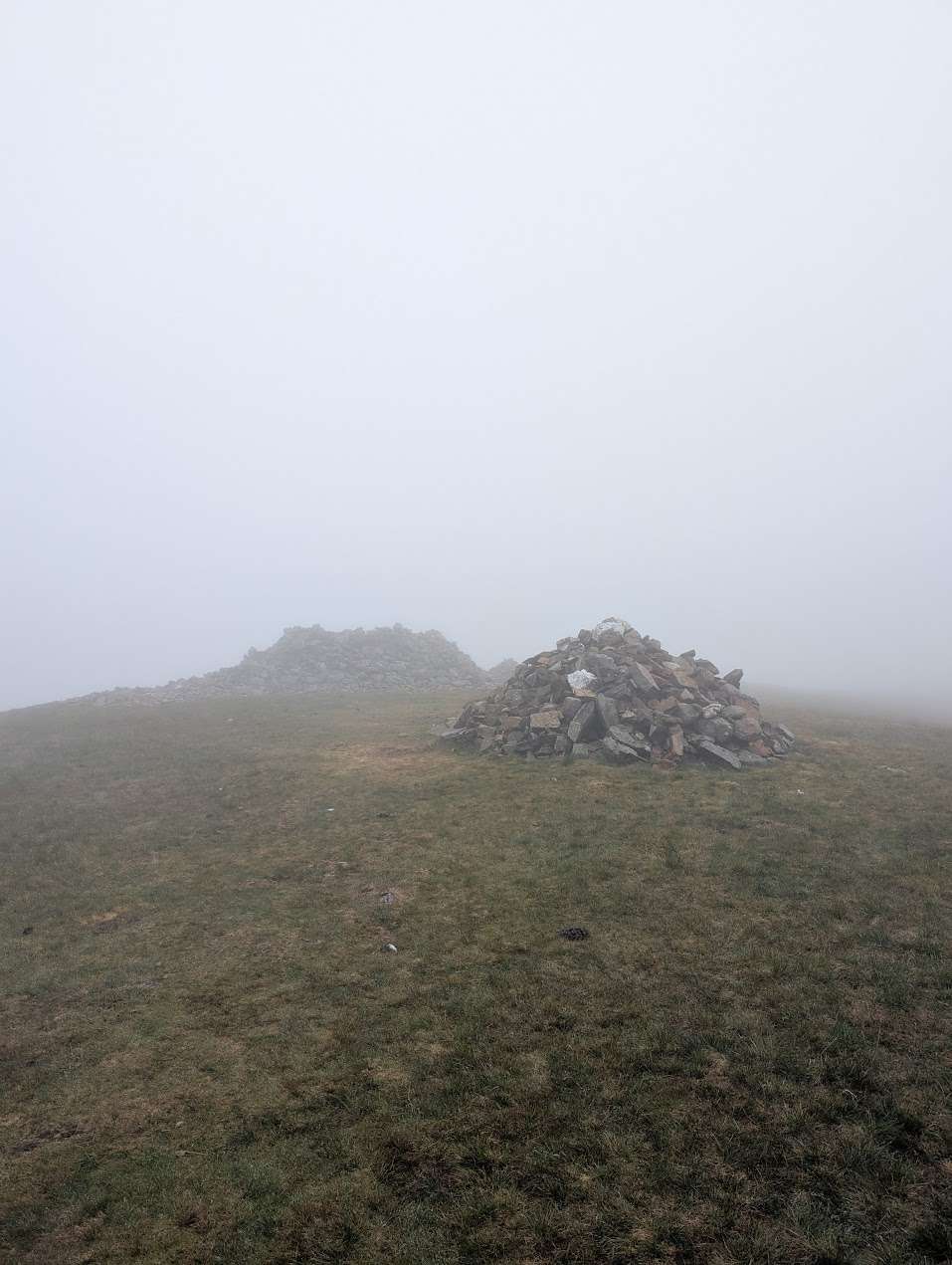 Grike - a stone cairn and a low shelter on a grassy summit, the view lost in thick mist