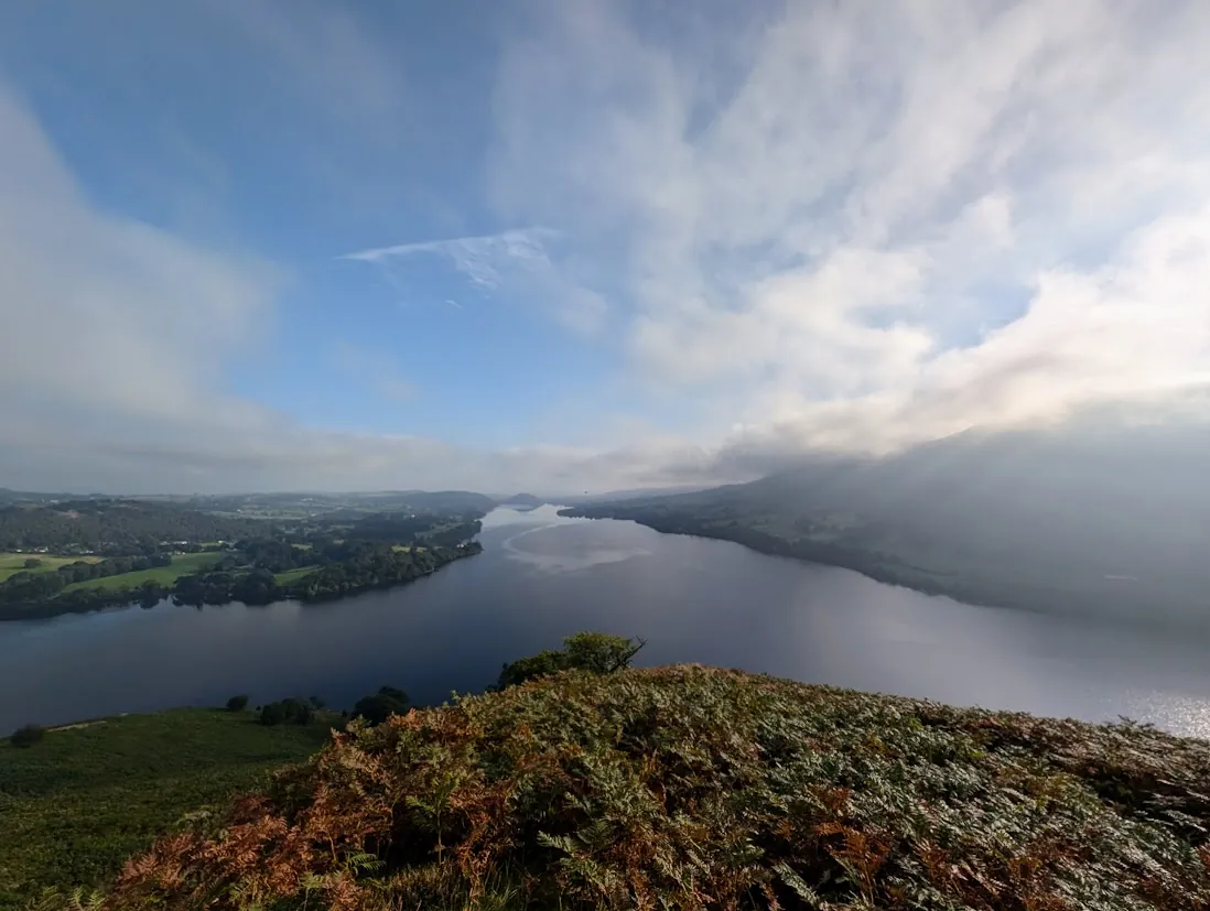 Hallin Fell - a grassy top with a cairn and a resting sheep, mist hanging over a mirror-calm Ullswater below