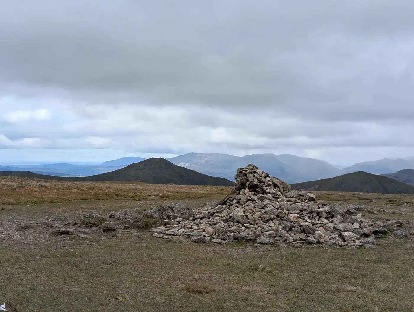 Harter Fell - a big summit cairn with old iron fence posts, rolling fells beyond under a grey cloudy sky