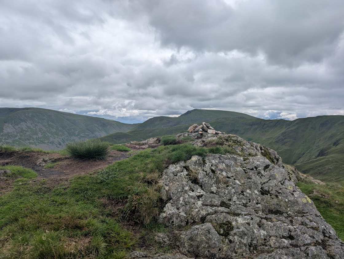 Hartsop above How - a small cairn on a rocky ridge, green fells rolling away beneath a grey cloudy sky