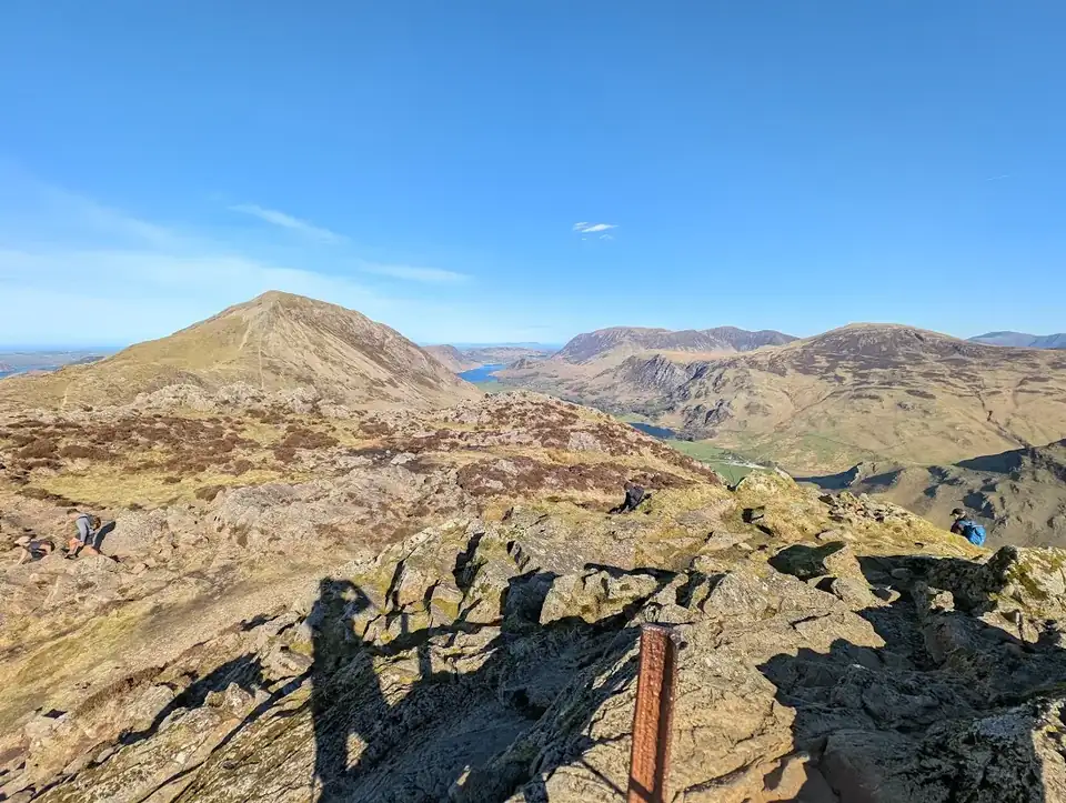 Haystacks - a rocky summit with an old fence post, Buttermere and Crummock Water glinting between fells under blue sky