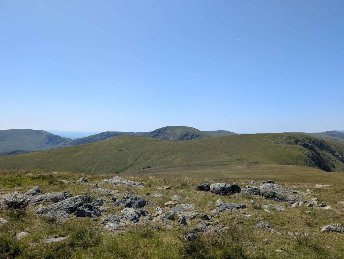 High Raise - a broad stony plateau looking across rolling grassy fells of the High Street range under deep blue sky
