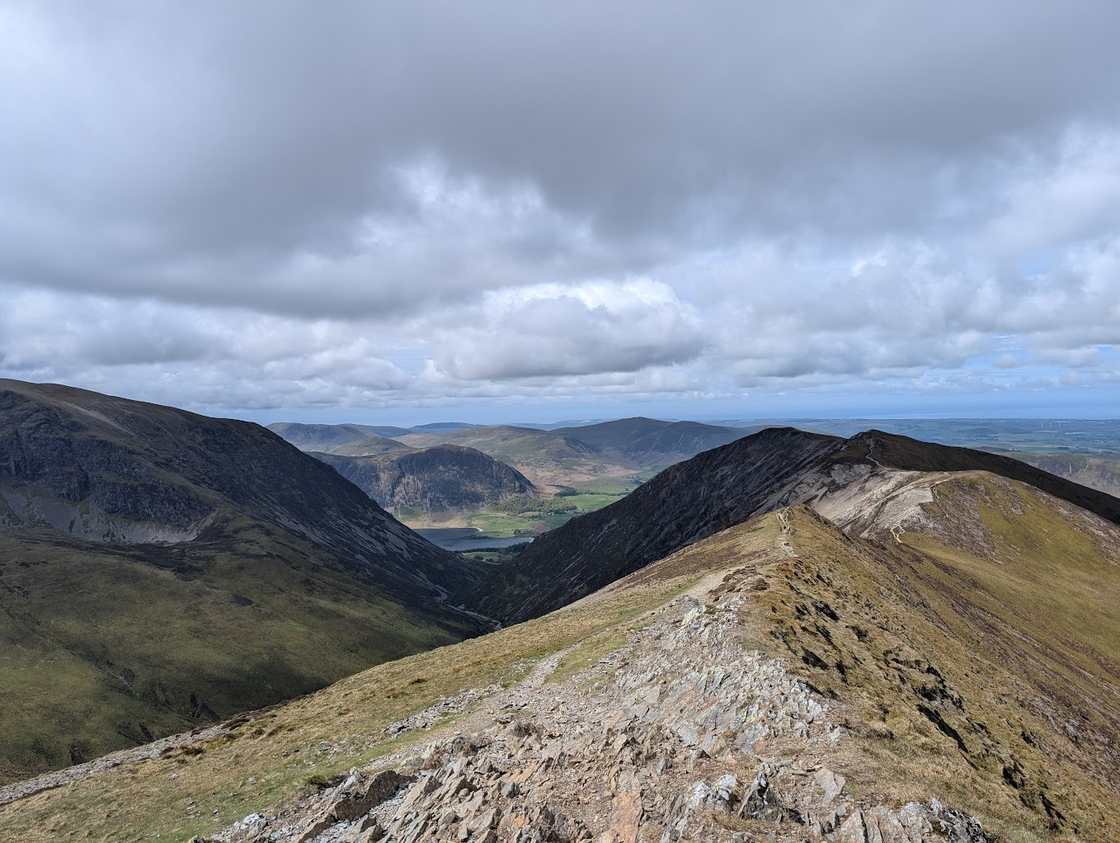 Hopegill Head - a sharp ridge curving above a deep valley, distant lowlands beyond under a grey cloudy sky