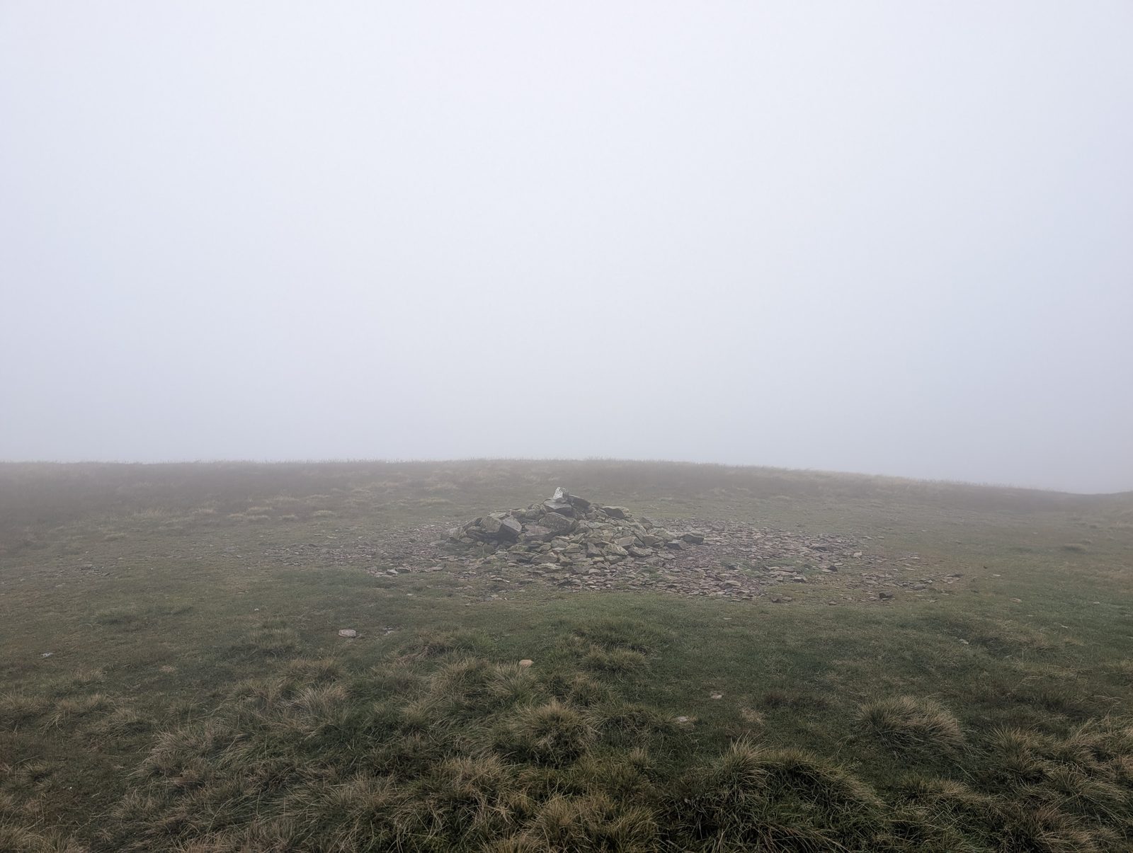 A low cairn of stones on Knott's broad, grassy summit, with mist hiding everything beyond.