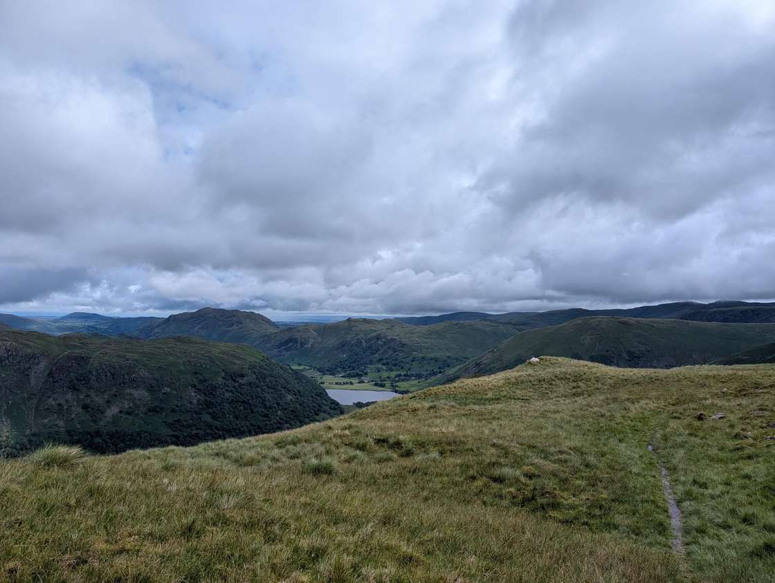Little Hart Crag - a grassy ridge above a green valley, Brothers Water below among the fells under heavy grey cloud