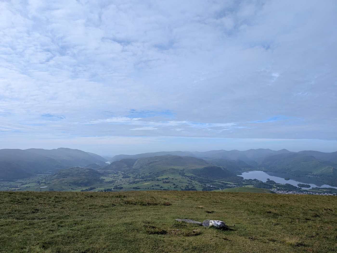 Lonscale Fell - a broad grassy top above a hazy sweep of fells and valleys, Derwentwater and Thirlmere glinting below