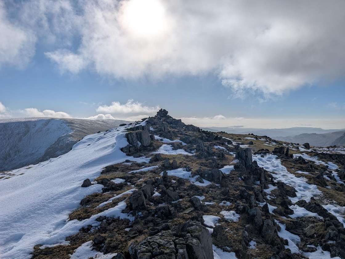 Mardale Ill Bell - a snow-streaked rocky summit and cairn, the winter sun behind cloud over hazy distant fells