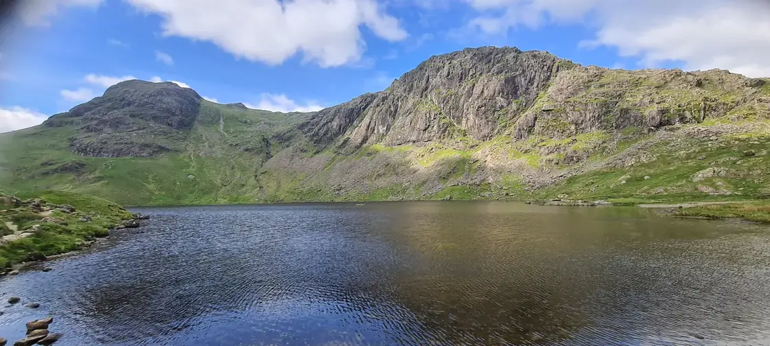 Pavey Ark - the great crag rising steeply behind Stickle Tarn, Harrison Stickle peaking to the left under blue sky