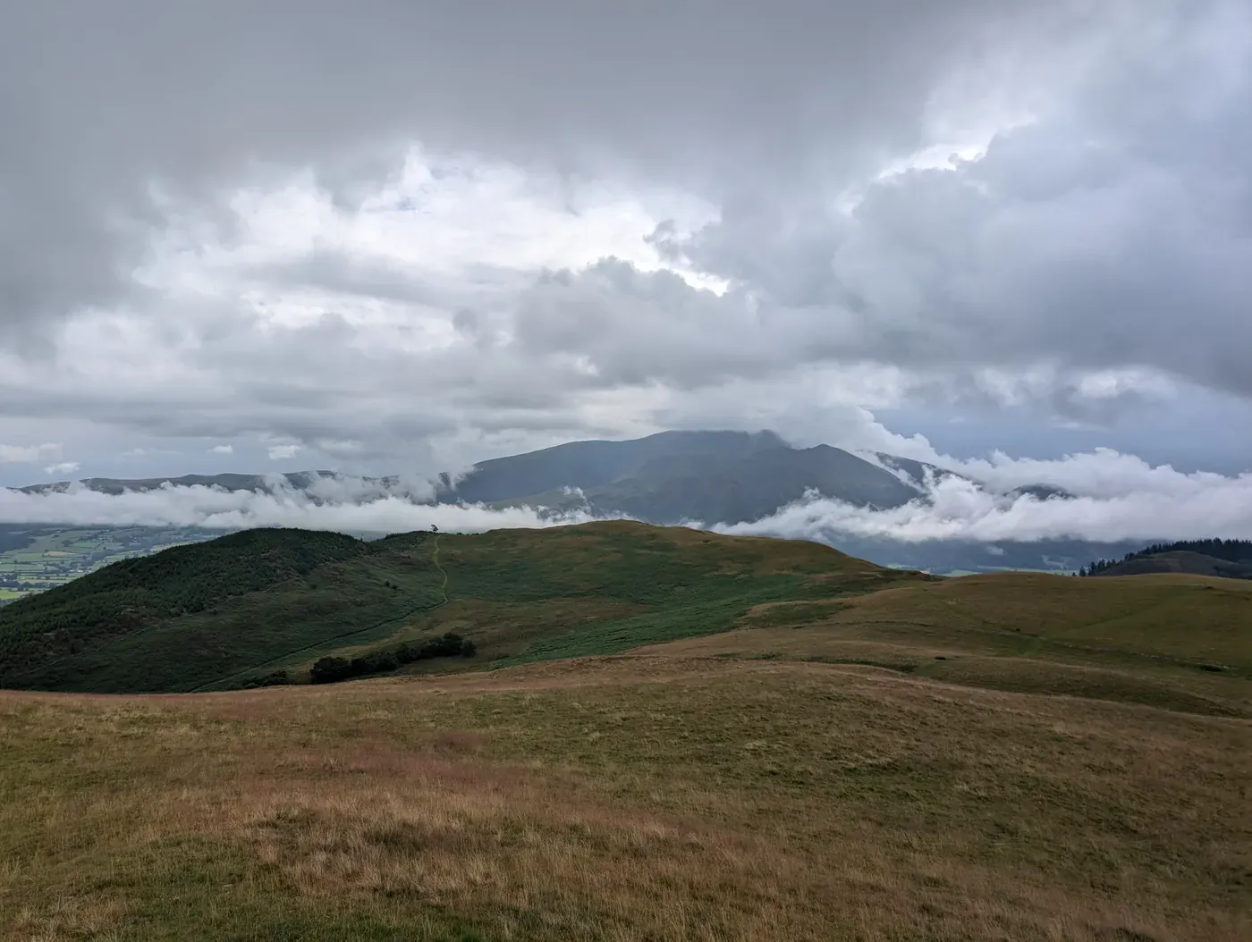 Sale Fell - rolling grassy slopes looking across to Skiddaw wreathed in cloud, low cloud banding the fells beyond
