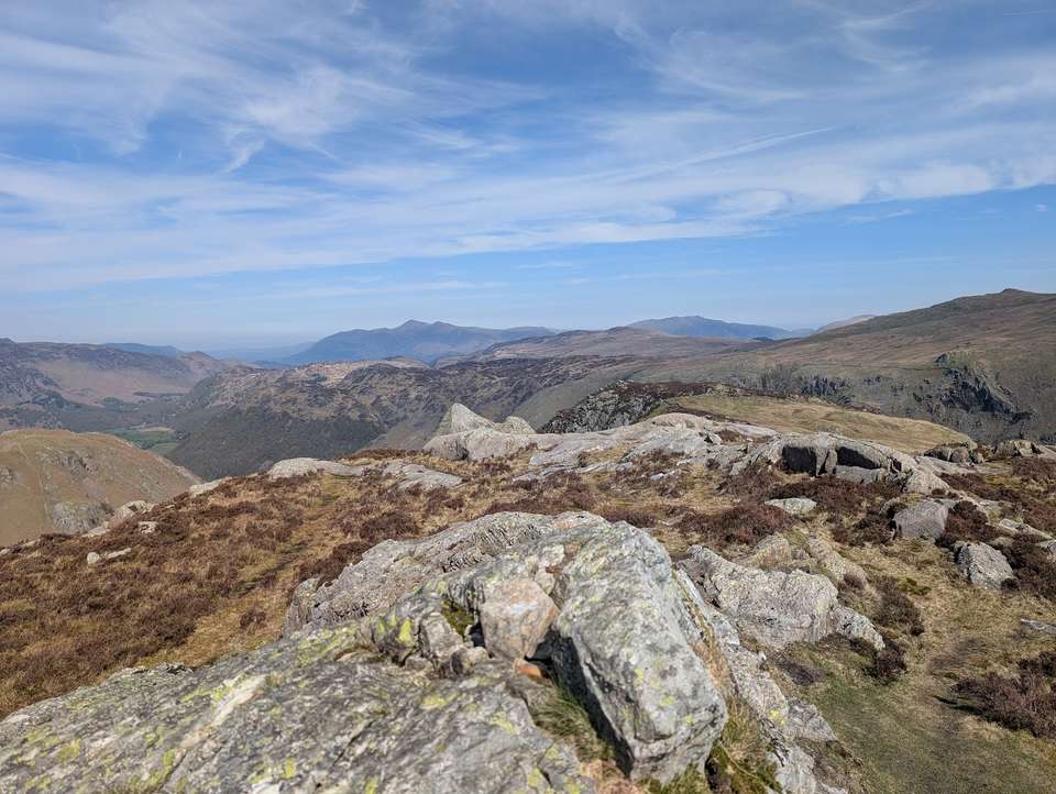 Sergeant's Crag - a rocky heathery top above a deep green valley, distant fells ranged across the horizon under blue sky