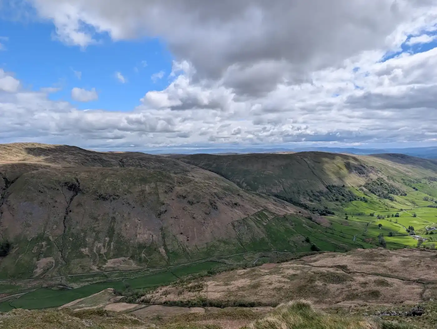 Shipman Knotts - grassy fellsides above a green valley of fields and walls, rolling fells under big clouds