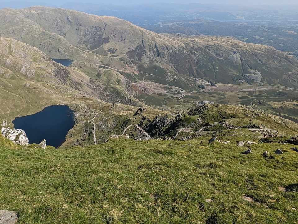 The Old Man of Coniston - a high view down to dark tarns and old quarry workings, paths winding among hazy fells