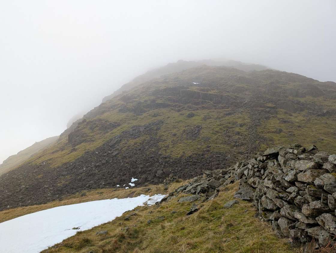 Threshtwaite Mouth - mist clinging to a craggy summit above stone walls and snow patches on the rocky slope