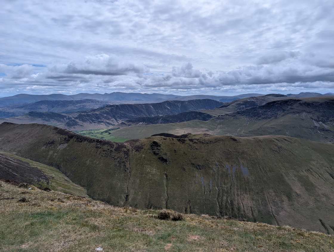 Wandope - a grassy edge above a deep crag-rimmed combe, rolling north-western fells receding under grey cloud