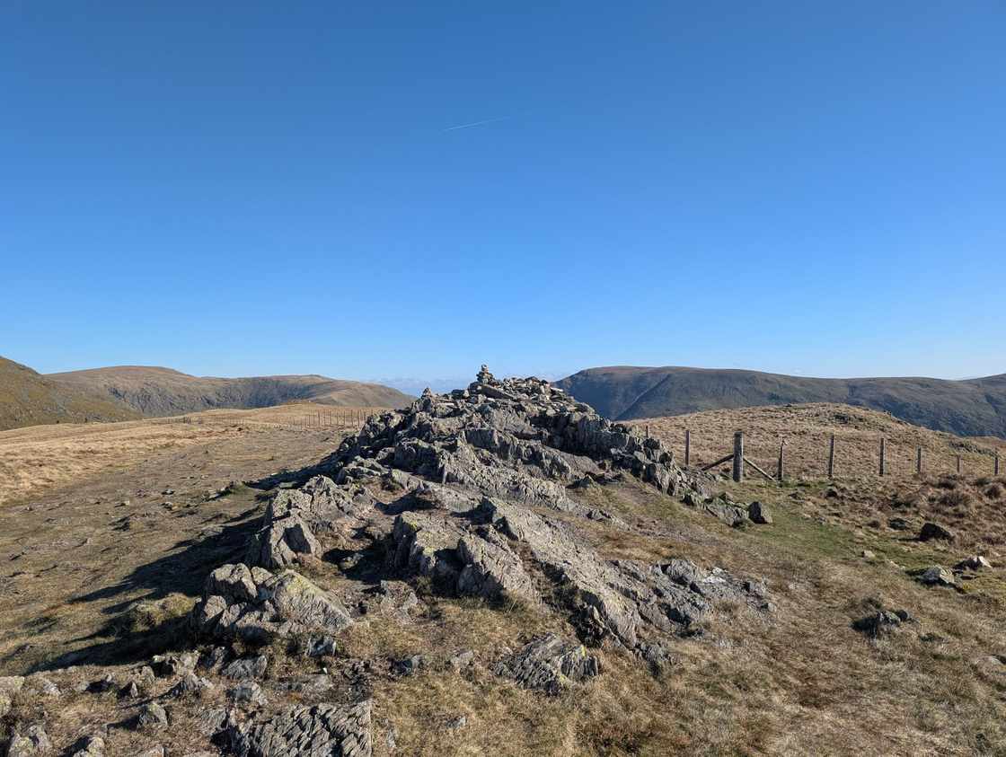 Yoke - a small cairn on a rocky outcrop with a fence line, rolling grassy fells beyond under clear deep-blue sky