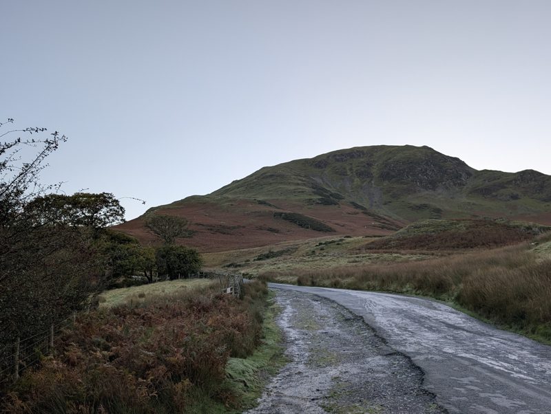 The Newlands Pass road above Buttermere with a rough verge beside it, a grassy fell rising ahead