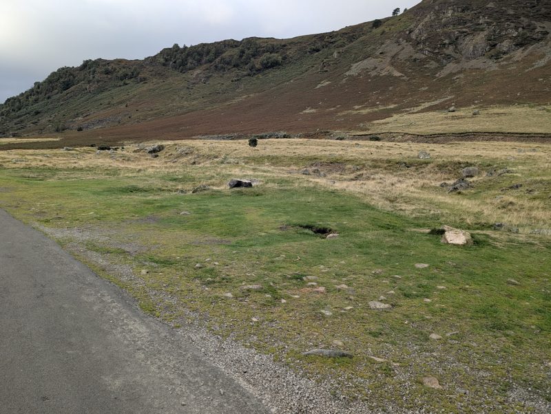 Open grassy ground beside the road below the crags of Carrock Fell