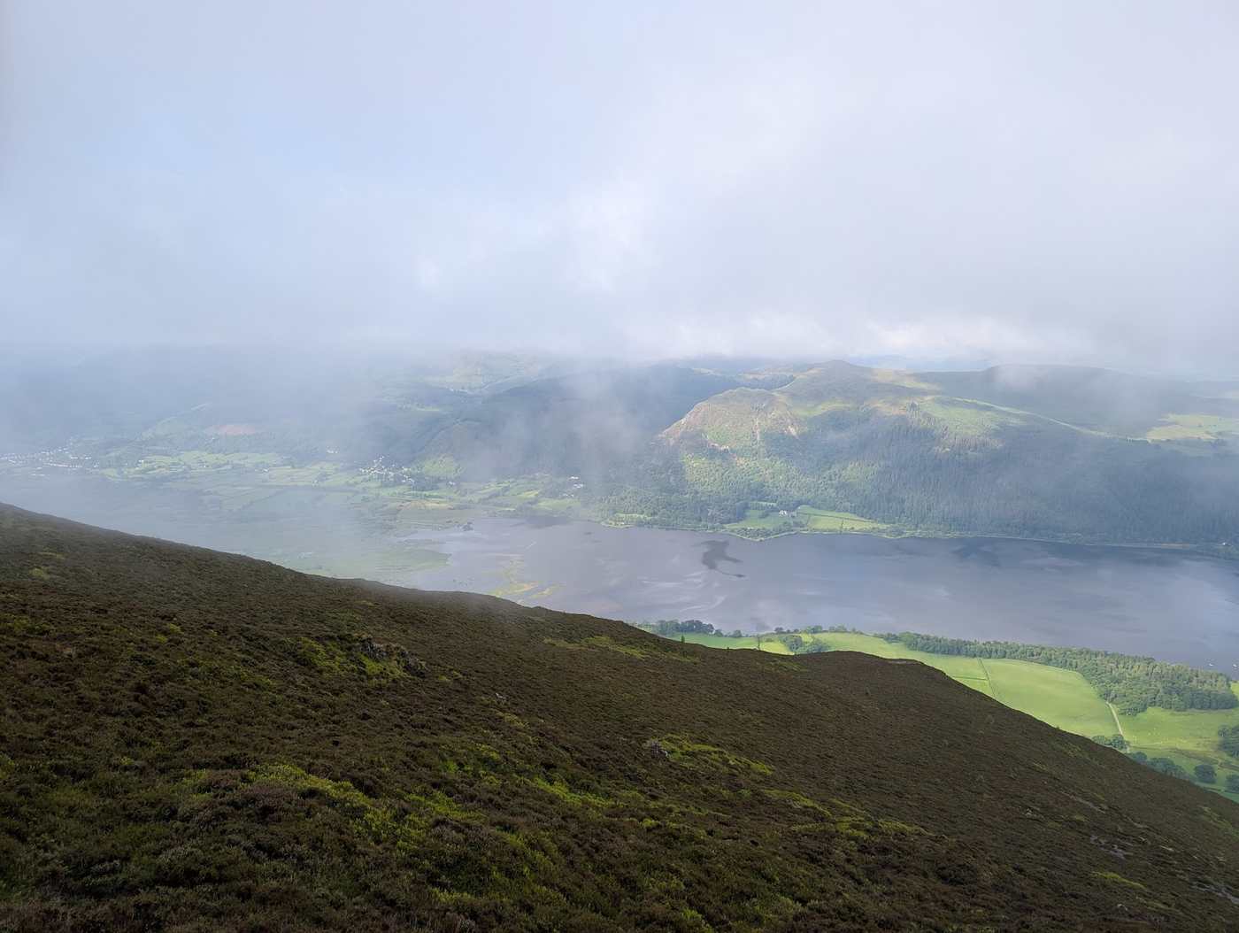 Bassenthwaite Lake below a heathery fellside, low cloud drifting over the forested far shore beneath Skiddaw