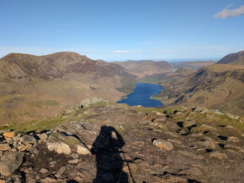 Buttermere and Crummock Water lying blue in their valley far below, seen over the rocky edge of a summit with fells rising on both sides
