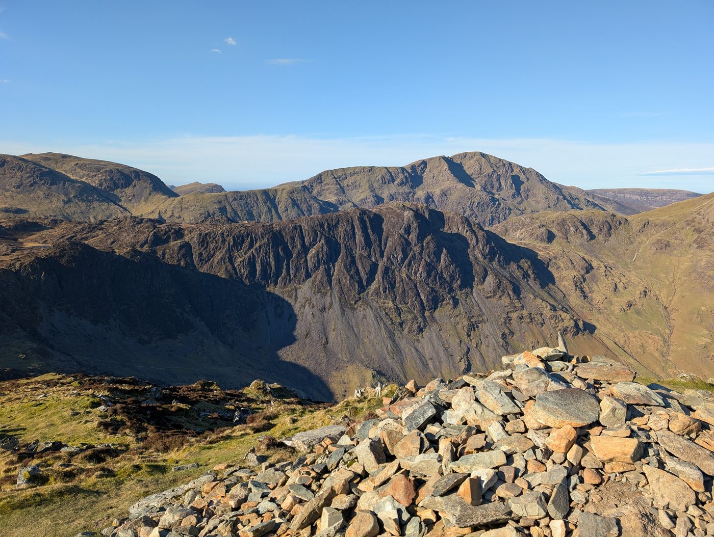 The summit cairn on Fleetwith Pike, with the craggy face of a big fell across the valley in clear April sunshine