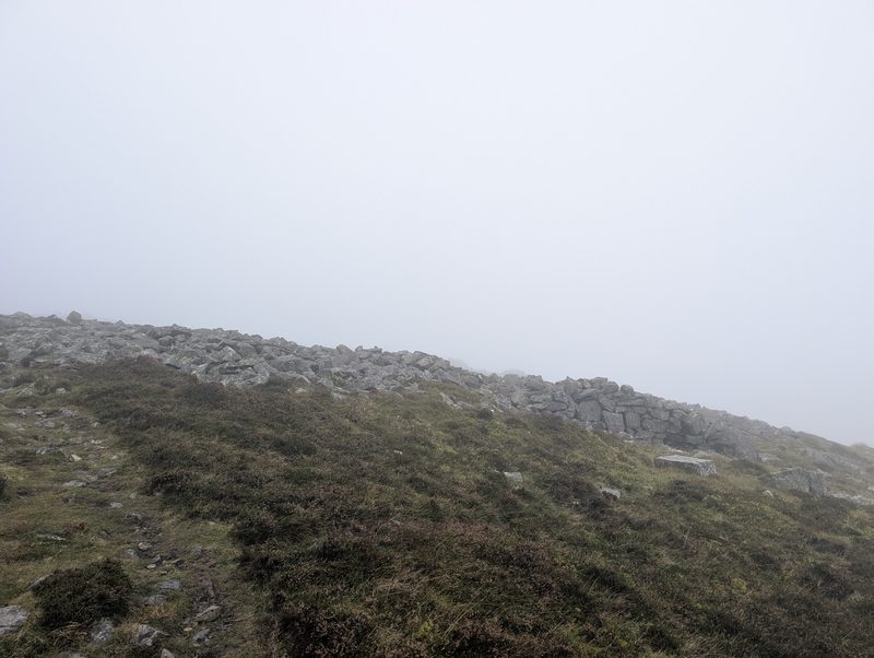 The tumbled stone wall of the hill fort on Carrock Fell, low along the skyline in mist