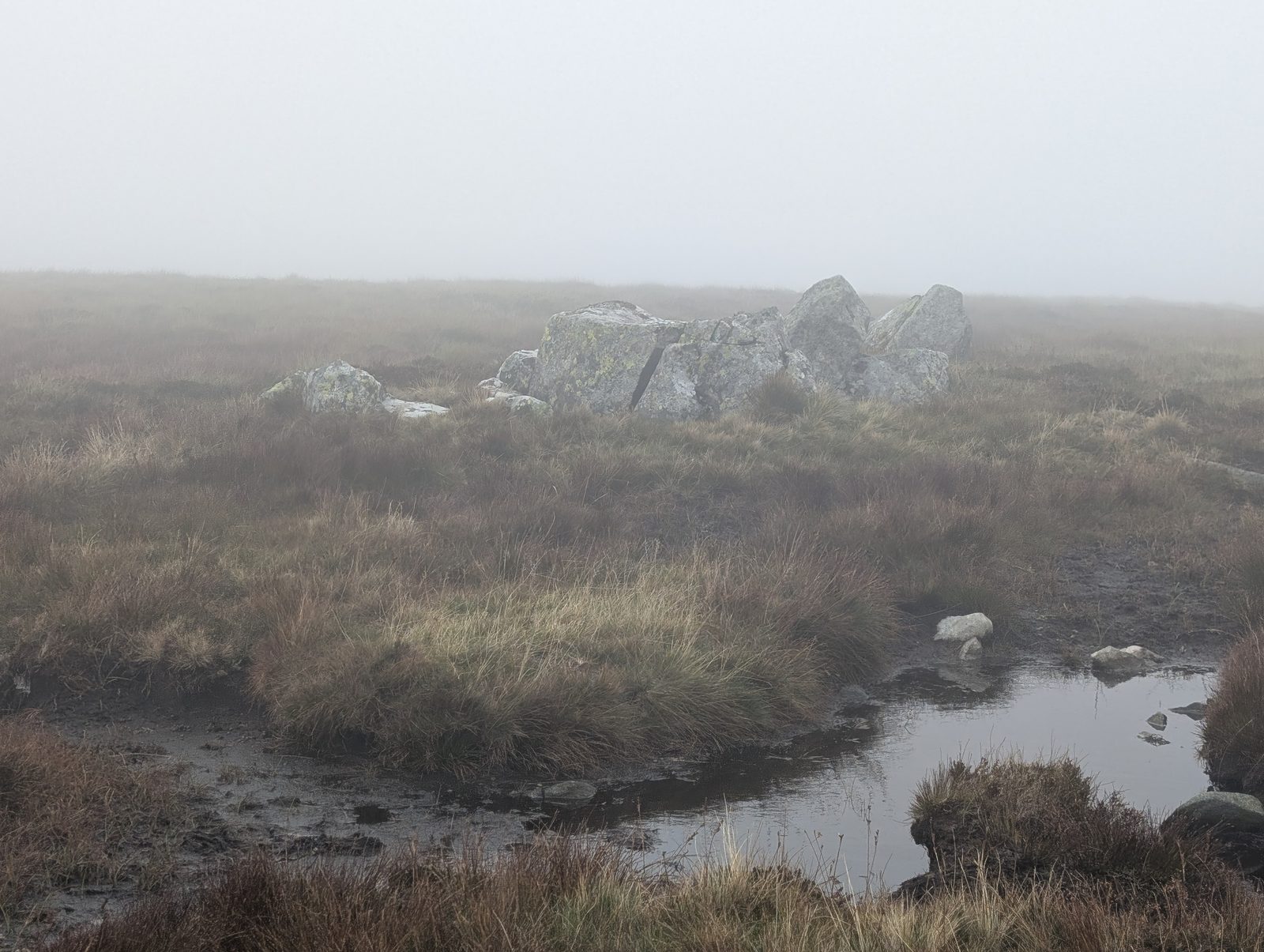 Grey boulders beside a peaty pool on the moor between Round Knott and Miton Hill, in mist