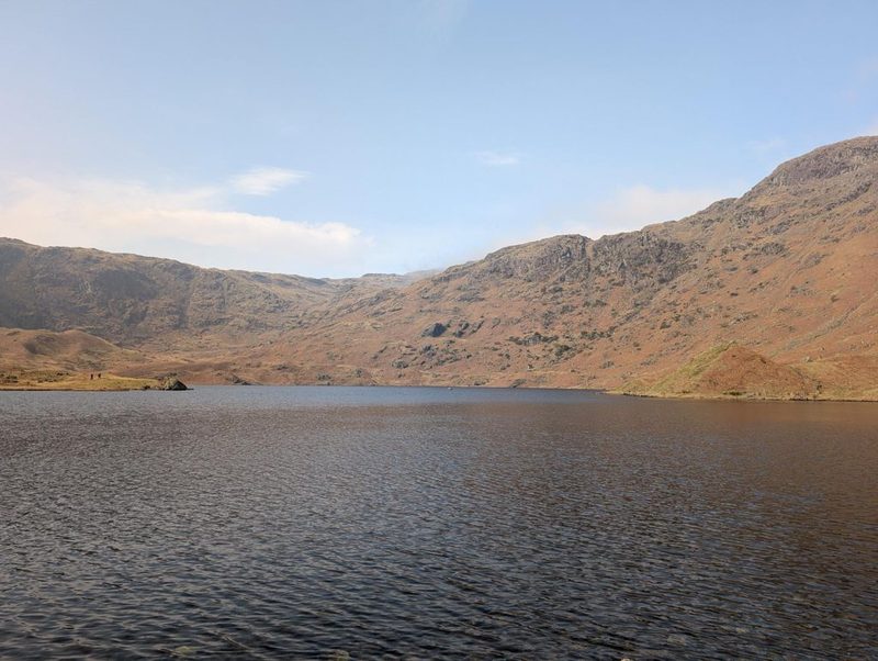 A large upland tarn ruffled by wind, with a broad crag-broken fellside in bracken-brown winter colour rising steeply beyond it