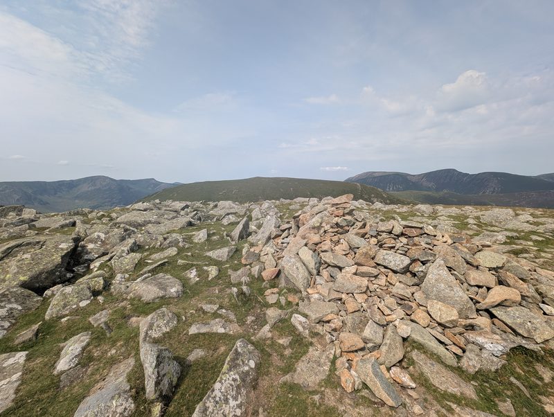The large stone cairn on the rocky summit of Hindscarth, with bare slabs and boulders around it and hazy fells ranged along the horizon