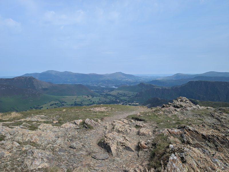 A stony path running over bare rock on the crest of a ridge, with the Newlands valley, Derwent Water and distant fells opening out ahead