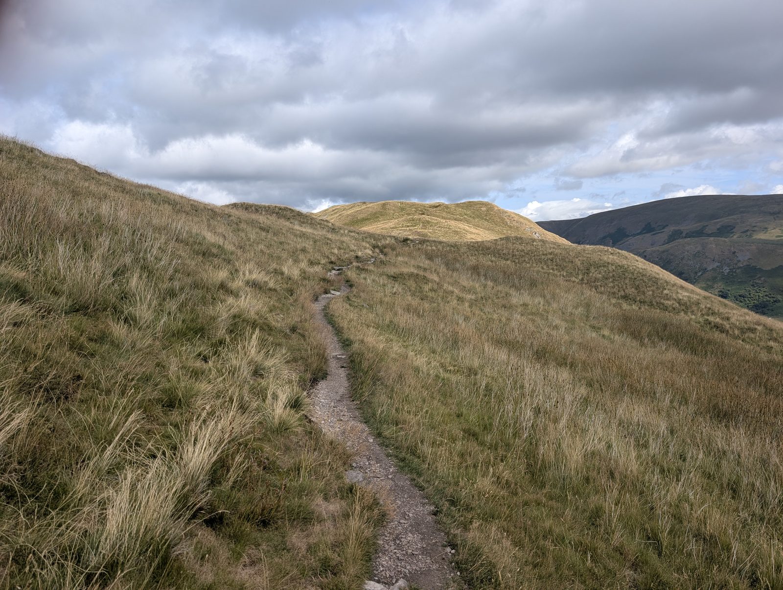 A grassy path running along the ridge from Beda Fell towards the next rounded top, the ground falling away to the valley on the left