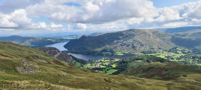 A large stone cairn on the broad grassy summit of Birkhouse Moor, with Ullswater and the low country stretching away beyond