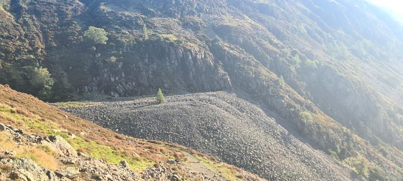 A cairn on a stony ridge crest looking across to a great crag-rimmed hollow, with a path climbing the skyline beyond