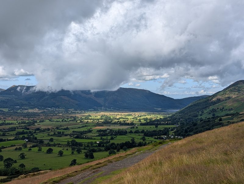 The Bassenthwaite valley from the descent, a patchwork of fields running north to the lake, with cloud spilling over the fells on the far side