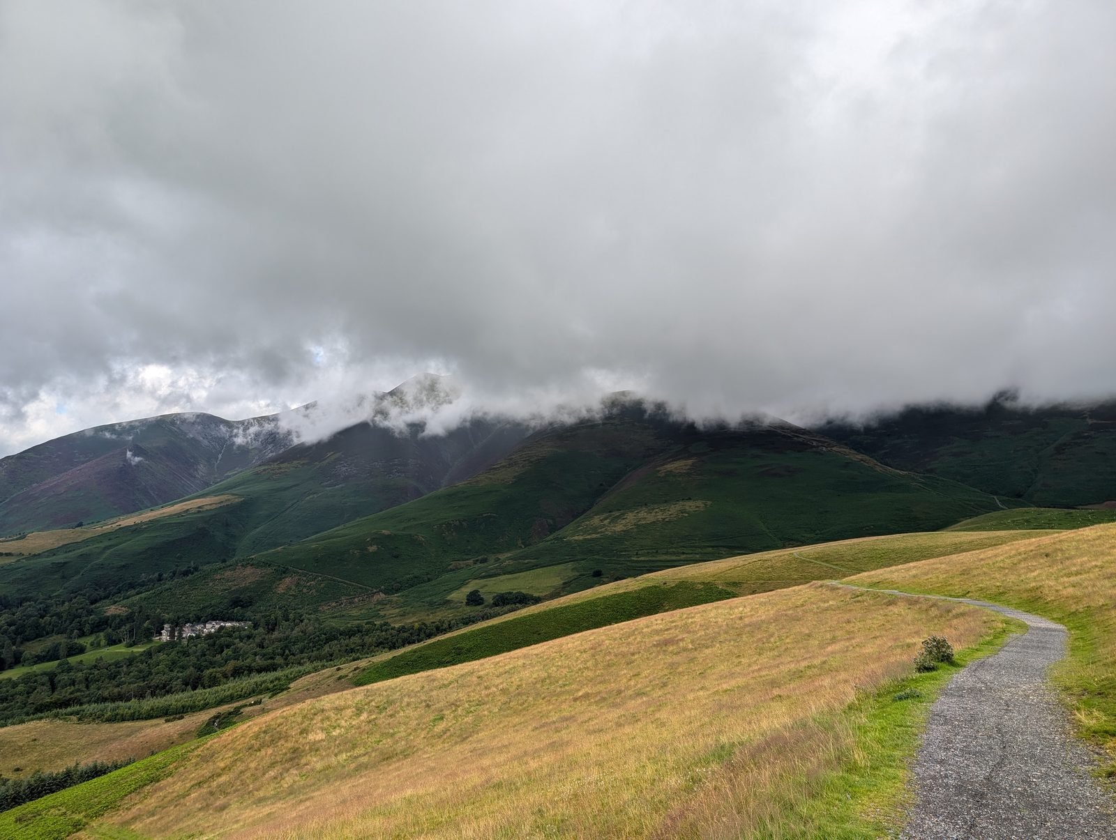 A gravel path curving along Latrigg's northern slope towards Skiddaw's green flanks, with low cloud cutting the tops off