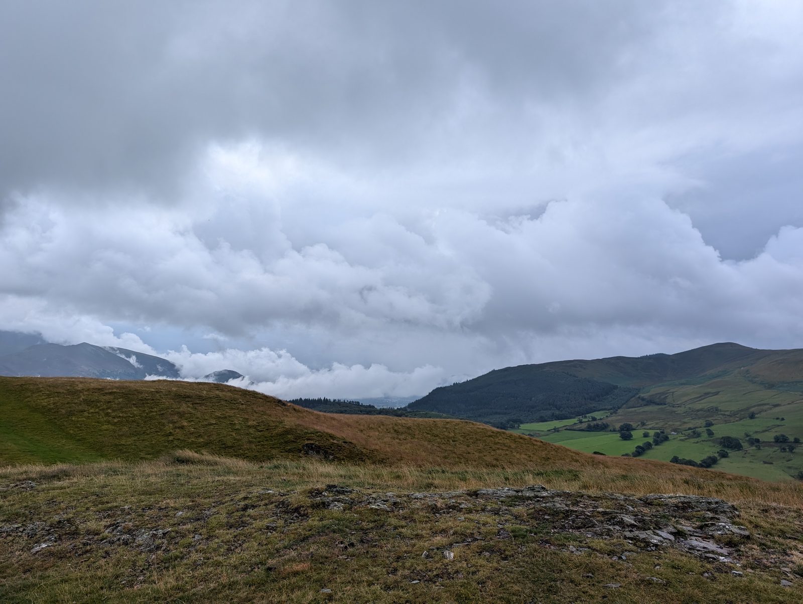 The rounded grassy top of Sale Fell, with cloud pouring over the Skiddaw fells and the green Wythop valley below