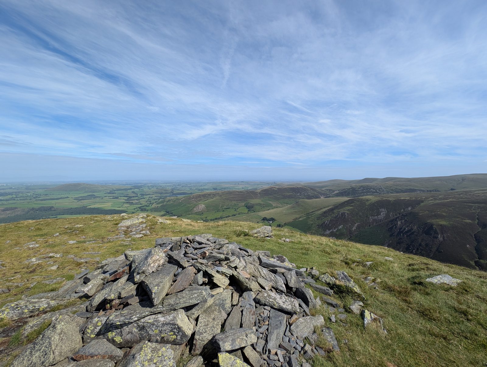 The summit cairn on Bakestall, a low pile of slate slabs, with the ground dropping away into the valley and the northern fells rolling away to the right