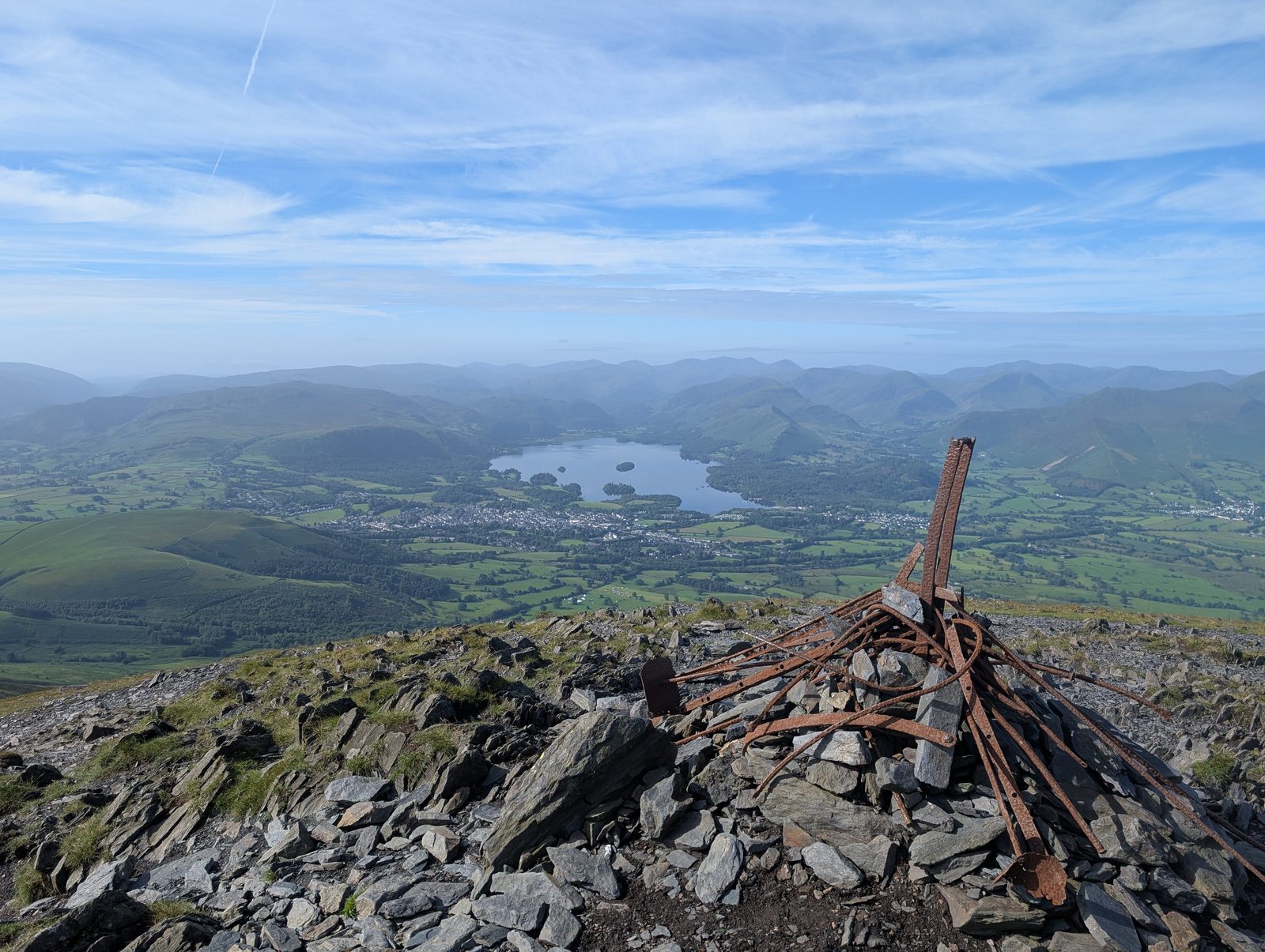 The rusted iron remains of an old fence post cluster on a stony summit, with Derwentwater, Keswick and the north-western fells spread out far below