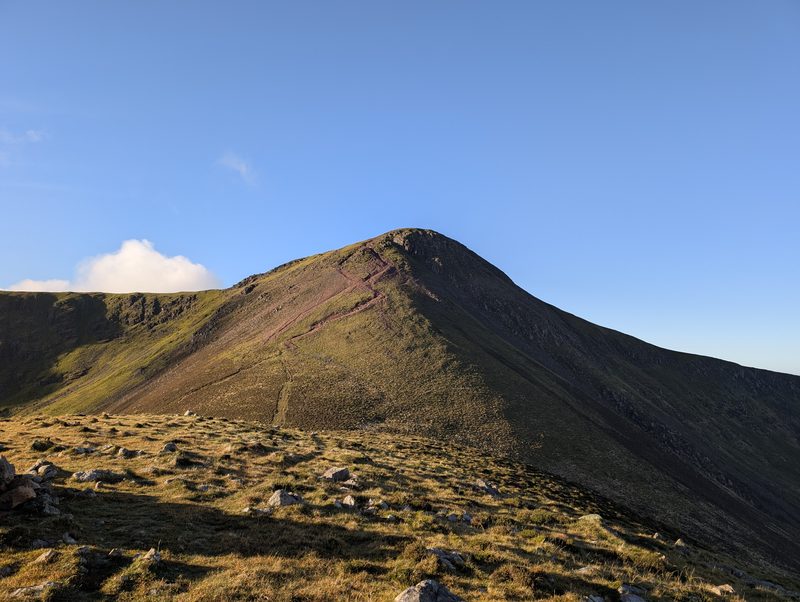 Red Pike seen from Dodd, a steep pointed top in shadow with a worn red path climbing its slope, under a clear blue sky