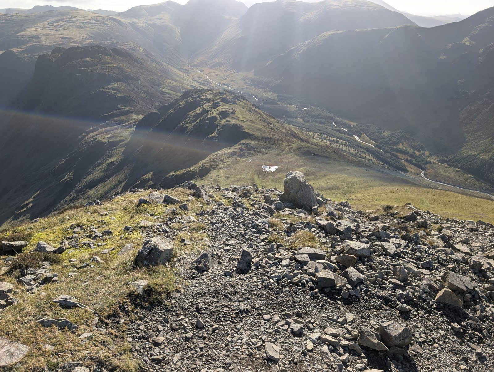 Loose grey stones at the top of Gamlin End, the ridge dropping away to Seat below and a valley with a river and forestry far below on the right