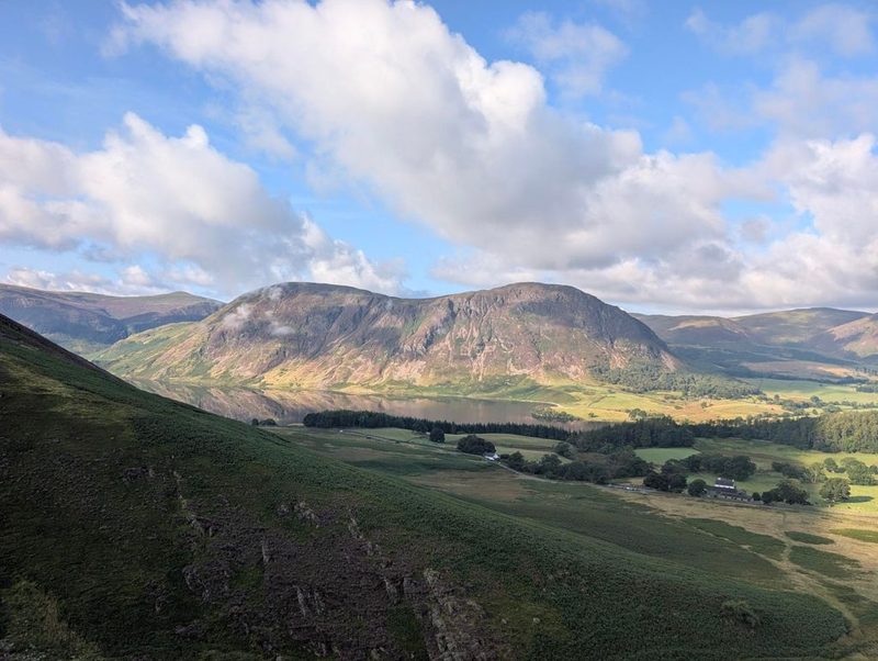 Looking back down over the green valley with its farms, walls and woods, and a line of fells catching the early sun along the far side